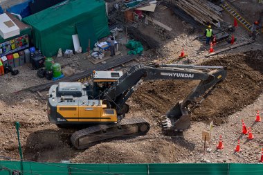 Sarı bir kazıcı, gücünü ve hassasiyetini kullanarak yüksek bir yapının gelecekteki temelini kazıyor. Gücün, ilerlemenin ve her büyük yapının arkasındaki enerjinin sembolü..