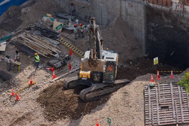 Sarı bir kazıcı, gücünü ve hassasiyetini kullanarak yüksek bir yapının gelecekteki temelini kazıyor. Gücün, ilerlemenin ve her büyük yapının arkasındaki enerjinin sembolü..
