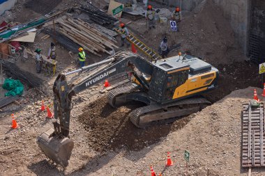 Sarı bir kazıcı, gücünü ve hassasiyetini kullanarak yüksek bir yapının gelecekteki temelini kazıyor. Gücün, ilerlemenin ve her büyük yapının arkasındaki enerjinin sembolü..
