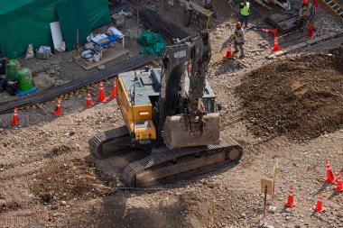Sarı bir kazıcı, gücünü ve hassasiyetini kullanarak yüksek bir yapının gelecekteki temelini kazıyor. Gücün, ilerlemenin ve her büyük yapının arkasındaki enerjinin sembolü..