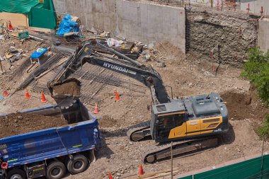 Hidrolik kazıcı aktif bir inşaat sahasında temel çalışması sırasında bir çöp kamyonuna toprak yüklerken ağır makineler iş başında,
