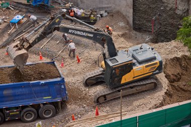 Hidrolik kazıcı aktif bir inşaat sahasında temel çalışması sırasında bir çöp kamyonuna toprak yüklerken ağır makineler iş başında,