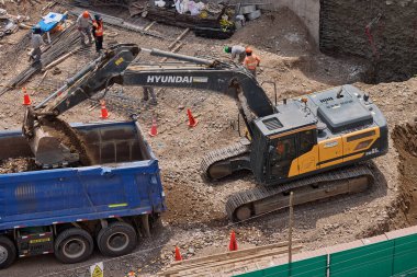 Hidrolik kazıcı aktif bir inşaat sahasında temel çalışması sırasında bir çöp kamyonuna toprak yüklerken ağır makineler iş başında,