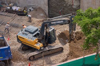 Hidrolik kazıcı aktif bir inşaat sahasında temel çalışması sırasında bir çöp kamyonuna toprak yüklerken ağır makineler iş başında,