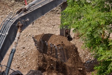 Kazı kovası kamyon yatağına ağır miktarda toprak boşaltıyor. Bu da inşaat alanındaki ilerlemenin sabit ritmine güç veriyor..