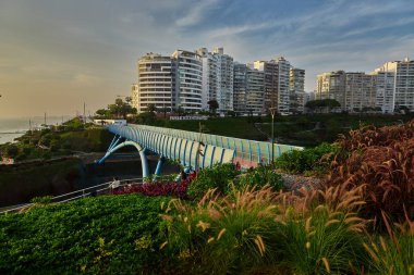 Lima, Miraflores 'teki Armendriz üzerindeki La Paz Köprüsü' nün modern manzarası, sahil binaları ve Pasifik boyunca gün batımı ışığı..
