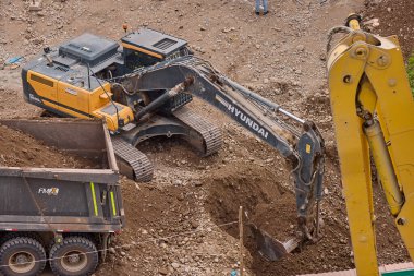 Hidrolik kazıcı aktif bir inşaat sahasında temel çalışması sırasında bir çöp kamyonuna toprak yüklerken ağır makineler iş başında