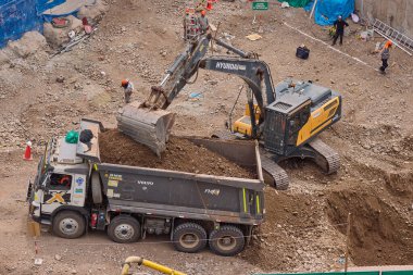 Hidrolik kazıcı aktif bir inşaat sahasında temel çalışması sırasında bir çöp kamyonuna toprak yüklerken ağır makineler iş başında