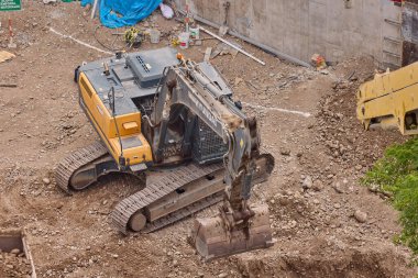 Hidrolik kazıcı aktif bir inşaat sahasında temel çalışması sırasında bir çöp kamyonuna toprak yüklerken ağır makineler iş başında