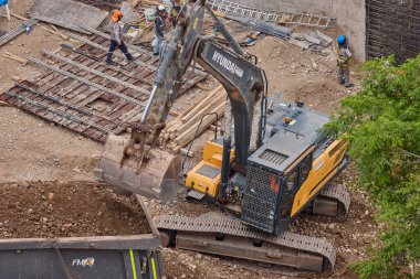 Hidrolik kazıcı aktif bir inşaat sahasında temel çalışması sırasında bir çöp kamyonuna toprak yüklerken ağır makineler iş başında,