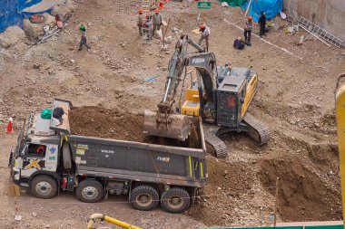 Hidrolik kazıcı aktif bir inşaat sahasında temel çalışması sırasında bir çöp kamyonuna toprak yüklerken ağır makineler iş başında,