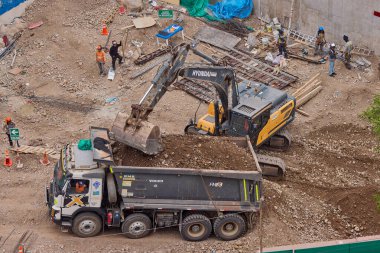 Hidrolik kazıcı aktif bir inşaat sahasında temel çalışması sırasında bir çöp kamyonuna toprak yüklerken ağır makineler iş başında,