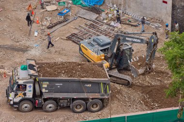 Hidrolik kazıcı aktif bir inşaat sahasında temel çalışması sırasında bir çöp kamyonuna toprak yüklerken ağır makineler iş başında,