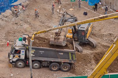 Hidrolik kazıcı aktif bir inşaat sahasında temel çalışması sırasında bir çöp kamyonuna toprak yüklerken ağır makineler iş başında,