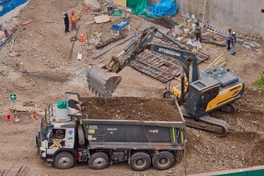 Hidrolik kazıcı aktif bir inşaat sahasında temel çalışması sırasında bir çöp kamyonuna toprak yüklerken ağır makineler iş başında,