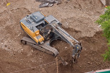 Hidrolik kazıcı aktif bir inşaat alanında temel çalışması sırasında bir çöp kamyonuna toprak yüklerken, ağır sarı makineler iş başında.,