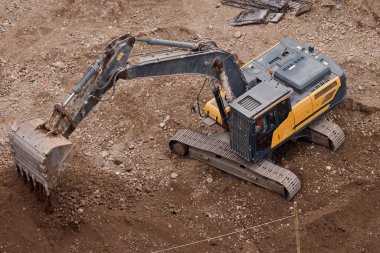 Hidrolik kazıcı aktif bir inşaat alanında temel çalışması sırasında bir çöp kamyonuna toprak yüklerken, ağır sarı makineler iş başında.,