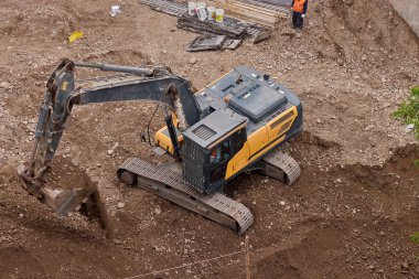 Hidrolik kazıcı aktif bir inşaat alanında temel çalışması sırasında bir çöp kamyonuna toprak yüklerken, ağır sarı makineler iş başında.,