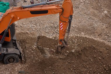 İki kazıcı, dinamik kazı ortamında işçiler, güvenlik ekipmanları ve yapısal malzemelerle çevrili bir inşaat sahasında aktif toprak taşımacılığı yapıyor..
