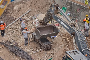 Hidrolik kazıcı aktif bir inşaat sahasında temel çalışması sırasında bir çöp kamyonuna toprak yüklerken ağır makineler iş başında,