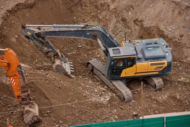 Sarı bir kazıcı, gücünü ve hassasiyetini kullanarak yüksek bir yapının gelecekteki temelini kazıyor. Gücün, ilerlemenin ve her büyük yapının arkasındaki enerjinin sembolü..