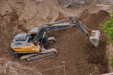 İnşaat alanında kazı yapan kazıcı, zemin ve temel hazırlıkları sırasında toprak ve kayaları hareket ettirdi..