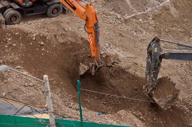İki kazıcı toprak ve kaya katmanlarını kazarak hareketlerini koordine ederek aktif bir inşaat projesinin temelini oluşturuyorlar..