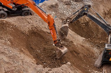 İki kazıcı toprak ve kaya katmanlarını kazarak hareketlerini koordine ederek aktif bir inşaat projesinin temelini oluşturuyorlar..