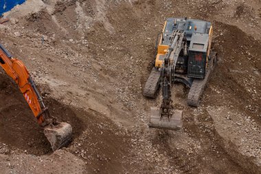 İki kazıcı toprak ve kaya katmanlarını kazarak hareketlerini koordine ederek aktif bir inşaat projesinin temelini oluşturuyorlar..