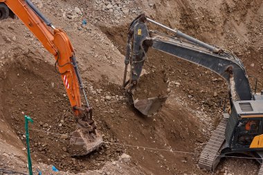 İki kazıcı toprak ve kaya katmanlarını kazarak hareketlerini koordine ederek aktif bir inşaat projesinin temelini oluşturuyorlar..