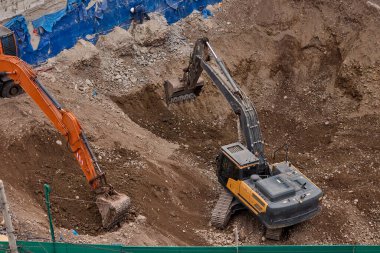 İki kazıcı toprak ve kaya katmanlarını kazarak hareketlerini koordine ederek aktif bir inşaat projesinin temelini oluşturuyorlar..