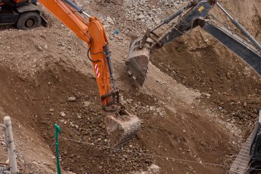 İki kazıcı toprak ve kaya katmanlarını kazarak hareketlerini koordine ederek aktif bir inşaat projesinin temelini oluşturuyorlar..