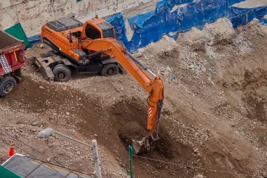 Bir kazıcı, inşaat sahasında devam eden toprak taşıma operasyonlarının bir parçası olarak, kovasını bir çöp kamyonunun üzerine yerleştirir..