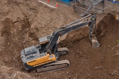 Sarı Kazıcı bir inşaat alanında kazı yapıyor, zemin ve temel hazırlıkları sırasında toprak ve kayaları hareket ettiriyor..