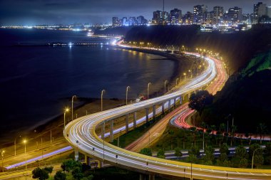 Uzun pozlu fotoğraf, Costa Verde (Yeşil Kıyı) otoyolunun Miraflores, Lima, Peru 'daki uçurumların eteklerinde esen dramatik kıvrımlarını yakalar. Görüntü şehrin modern altyapısını vurguluyor