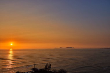 Malecn de Miraflores 'den çarpıcı bir yaz akşamı manzarası, doğrudan kıyı uçurumlarına inşa edilen tek Güney Amerika başkenti. Görüntü, canlı turuncu ve mor renklerin Pasifik Okyanusu 'na yansıdığı dramatik bir gün batımı yakalıyor..