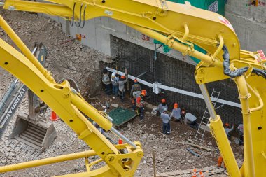 Yüksek binadaki İnşaat İşçileri İnşaat Vakfı. Ağır makinelerin sarı kolları tarafından çerçevelenmiş bir bina temeli üzerinde çalışan pek çok inşaat işçisi..
