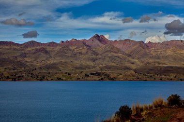Cusco 'nun Espinar kenti yakınlarındaki Canas ilinde bulunan Langui Layo lagünü, parlak bir gökyüzü ve beyaz bulutları yansıtan derin mavi sulara sahip. Çevresindeki And manzarası altın dağlık araziler, küçük kırsal yerleşim alanları ve bir arkaplan