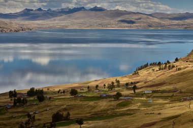 Cusco 'nun Espinar kenti yakınlarındaki Canas ilinde bulunan Langui Layo lagünü, parlak bir gökyüzü ve beyaz bulutları yansıtan derin mavi sulara sahip. Çevresindeki And manzarası altın dağlık araziler, küçük kırsal yerleşim alanları ve bir arkaplan