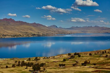 Cusco 'nun Espinar kenti yakınlarındaki Canas ilinde bulunan Langui Layo lagünü, parlak bir gökyüzü ve beyaz bulutları yansıtan derin mavi sulara sahip. Çevresindeki And manzarası altın dağlık araziler, küçük kırsal yerleşim alanları ve bir arkaplan