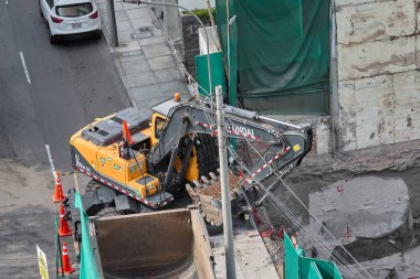 Kazıcı, Miraflores, Lima, Peru 'da kapalı bir kentsel inşaat sahasındaki bir kamyona toprak yüklüyor. Yoğun bir şehir ortamında ağır makine çalışması, mühendislik hassasiyeti ve devam eden kentsel gelişimi gösteriyor.