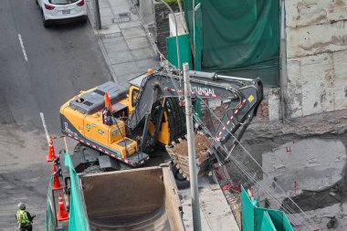 Kazıcı, Miraflores, Lima, Peru 'da kapalı bir kentsel inşaat sahasındaki bir kamyona toprak yüklüyor. Yoğun bir şehir ortamında ağır makine çalışması, mühendislik hassasiyeti ve devam eden kentsel gelişimi gösteriyor.