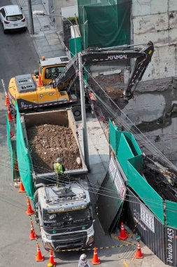Kazıcı, Miraflores, Lima, Peru 'da kapalı bir kentsel inşaat sahasındaki bir kamyona toprak yüklüyor. Yoğun bir şehir ortamında ağır makine çalışması, mühendislik hassasiyeti ve devam eden kentsel gelişimi gösteriyor.