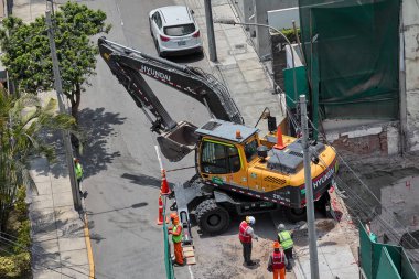 Kazıcı, Miraflores, Lima, Peru 'da kapalı bir kentsel inşaat sahasındaki bir kamyona toprak yüklüyor. Yoğun bir şehir ortamında ağır makine çalışması, mühendislik hassasiyeti ve devam eden kentsel gelişimi gösteriyor.