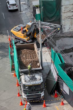 Kazıcı, Miraflores, Lima, Peru 'da kapalı bir kentsel inşaat sahasındaki bir kamyona toprak yüklüyor. Yoğun bir şehir ortamında ağır makine çalışması, mühendislik hassasiyeti ve devam eden kentsel gelişimi gösteriyor.