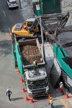 Kazıcı, Miraflores, Lima, Peru 'da kapalı bir kentsel inşaat sahasındaki bir kamyona toprak yüklüyor. Yoğun bir şehir ortamında ağır makine çalışması, mühendislik hassasiyeti ve devam eden kentsel gelişimi gösteriyor.