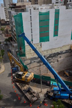 Ağır vinç kazıcıyı şehir ortamında derin bir inşaat sahasına kaldırıyor, altyapı geliştirme, gayrimenkul büyümesi ve modern şehir genişlemesi sergiliyor..