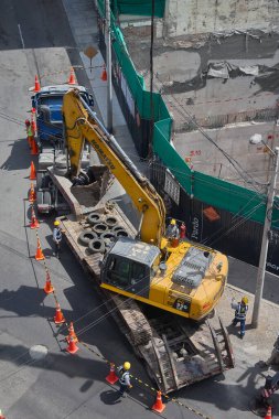 Ağır vinç kazıcıyı şehir ortamında derin bir inşaat sahasına kaldırıyor, altyapı geliştirme, gayrimenkul büyümesi ve modern şehir genişlemesi sergiliyor..