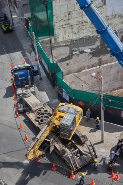 Ağır vinç kazıcıyı şehir ortamında derin bir inşaat sahasına kaldırıyor, altyapı geliştirme, gayrimenkul büyümesi ve modern şehir genişlemesi sergiliyor..