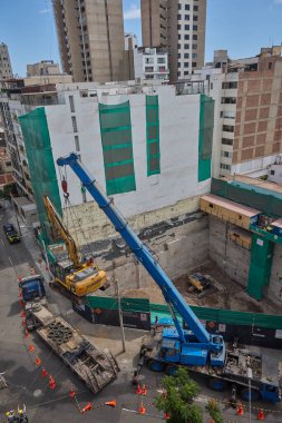 Ağır vinç kazıcıyı şehir ortamında derin bir inşaat sahasına kaldırıyor, altyapı geliştirme, gayrimenkul büyümesi ve modern şehir genişlemesi sergiliyor..